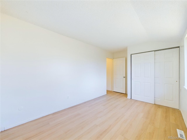 unfurnished bedroom with light wood-type flooring, a closet, and a textured ceiling