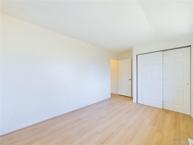 unfurnished bedroom featuring light hardwood / wood-style floors, a textured ceiling, a closet, and lofted ceiling