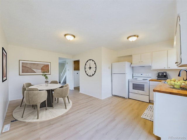 kitchen with butcher block counters, white appliances, light wood-type flooring, white cabinets, and sink