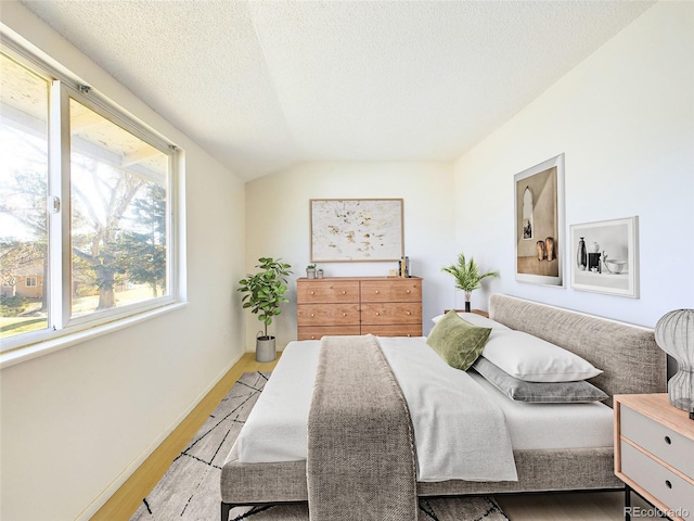 bedroom featuring light hardwood / wood-style floors, a textured ceiling, and lofted ceiling