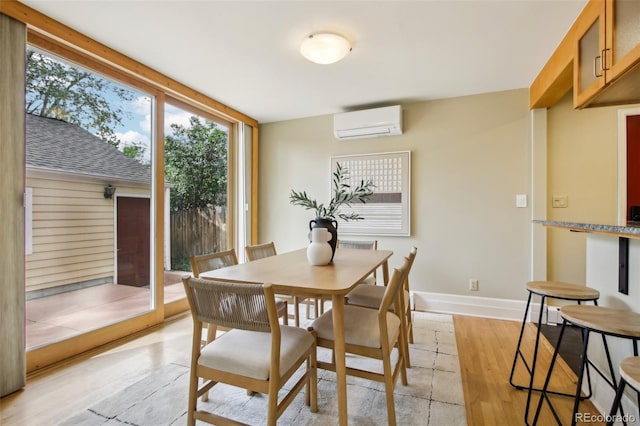dining room with an AC wall unit, light wood-style floors, plenty of natural light, and baseboards