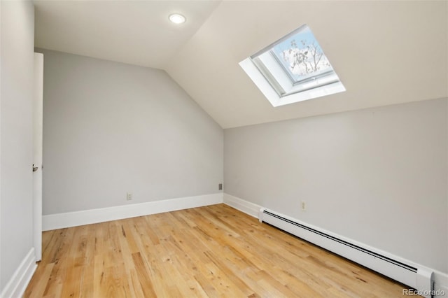 additional living space featuring baseboard heating, a skylight, vaulted ceiling, wood finished floors, and baseboards