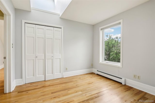 unfurnished bedroom with baseboard heating, light wood-style flooring, baseboards, and a closet