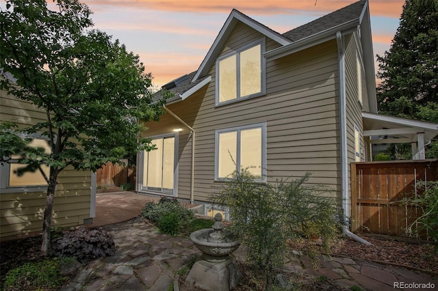 back of house at dusk with fence, a patio area, and roof with shingles