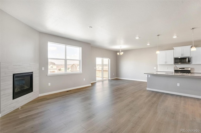 unfurnished living room with a textured ceiling, a chandelier, and light hardwood / wood-style floors