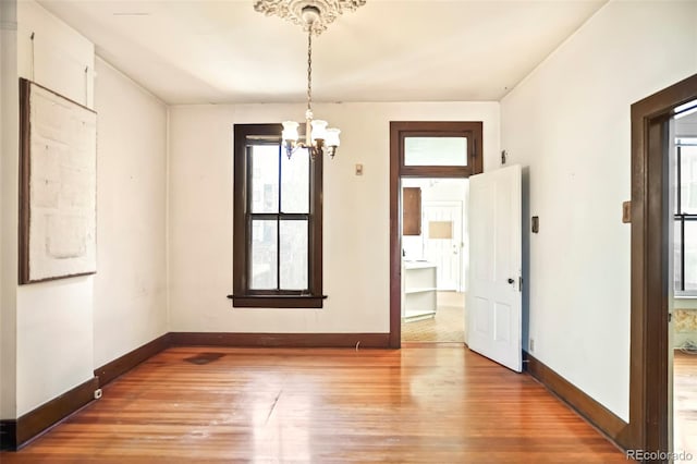 unfurnished room with baseboards, wood finished floors, and a notable chandelier