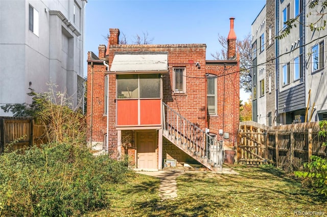 rear view of house featuring brick siding, fence, a sunroom, stairs, and a yard