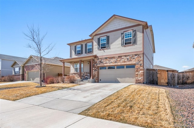 view of front of home with stone siding, covered porch, concrete driveway, and fence