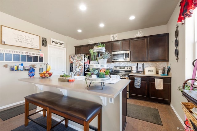 kitchen with dark brown cabinetry, appliances with stainless steel finishes, light countertops, and a kitchen breakfast bar