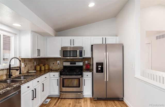 kitchen featuring lofted ceiling, sink, white cabinetry, stainless steel appliances, and dark stone counters