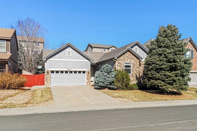 view of front of home featuring concrete driveway, board and batten siding, fence, a garage, and stone siding