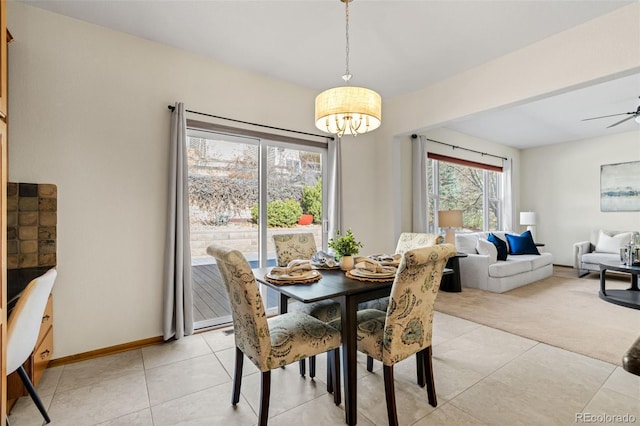 dining area with light carpet, ceiling fan with notable chandelier, light tile patterned flooring, and baseboards