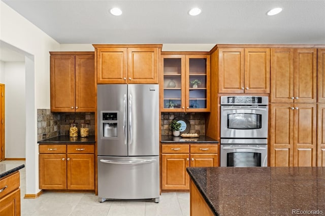 kitchen featuring stainless steel appliances, brown cabinetry, and dark stone countertops