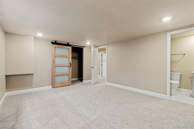 unfurnished bedroom with a closet, light colored carpet, a textured ceiling, ensuite bath, and baseboards