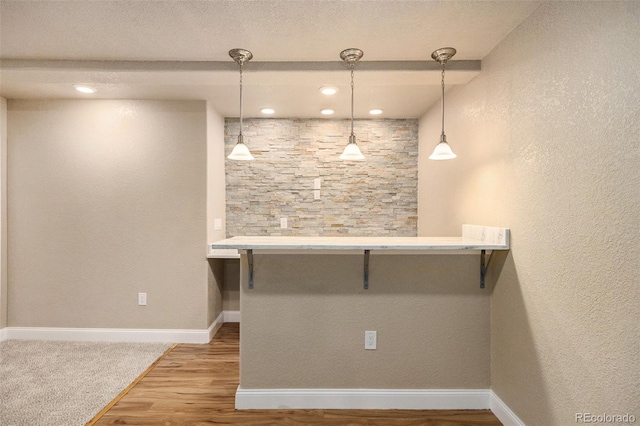 interior space featuring a textured wall, hanging light fixtures, baseboards, and wood finished floors