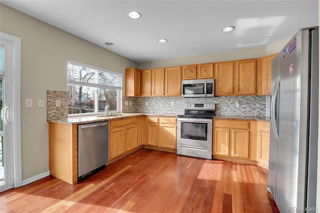 kitchen with sink, light hardwood / wood-style flooring, stainless steel appliances, light stone counters, and tasteful backsplash