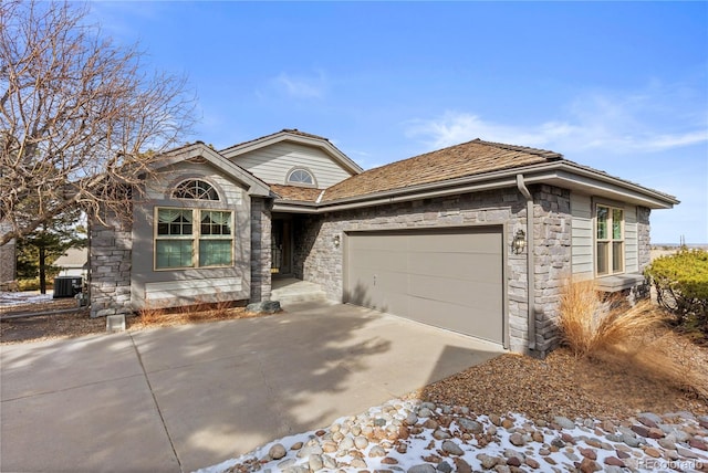 ranch-style house featuring concrete driveway, a garage, central AC unit, and stone siding