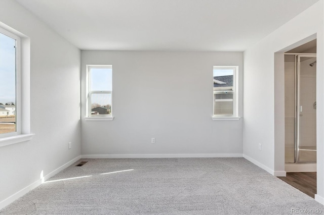 unfurnished bedroom featuring multiple windows, ensuite bath, and dark carpet