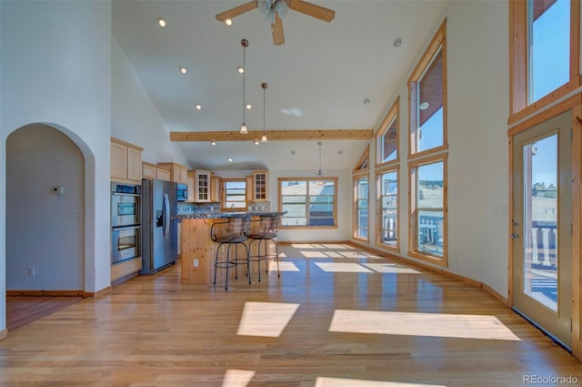 kitchen with appliances with stainless steel finishes, high vaulted ceiling, a kitchen island, a kitchen bar, and decorative light fixtures