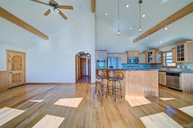 kitchen with light hardwood / wood-style floors, beam ceiling, appliances with stainless steel finishes, light brown cabinetry, and stone countertops