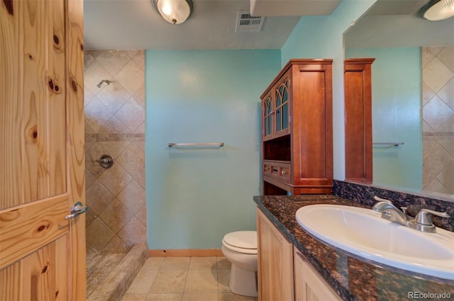 bathroom with tiled shower, tile patterned flooring, vanity, and toilet