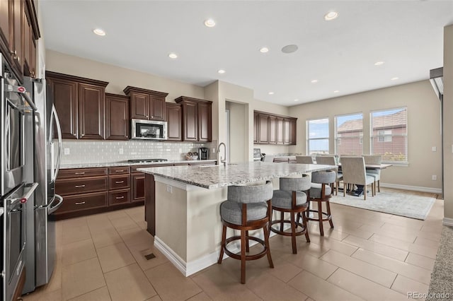 kitchen featuring light stone counters, stainless steel appliances, tasteful backsplash, a kitchen island with sink, and a kitchen breakfast bar