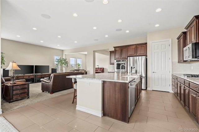 kitchen featuring light stone counters, a kitchen breakfast bar, backsplash, a center island with sink, and appliances with stainless steel finishes