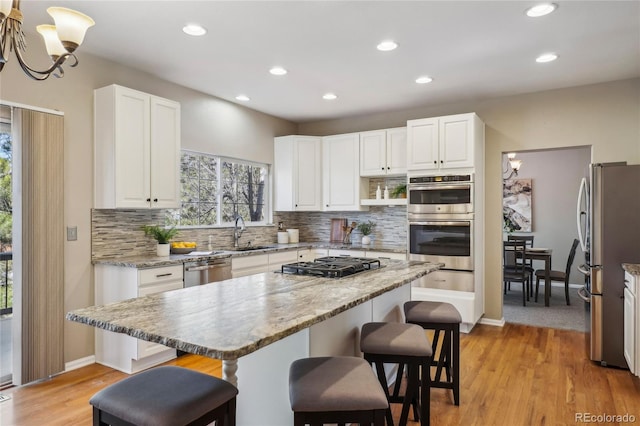 kitchen featuring white cabinets, appliances with stainless steel finishes, a kitchen breakfast bar, backsplash, and a sink