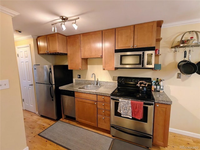 kitchen with appliances with stainless steel finishes, a sink, ornamental molding, light wood-style flooring, and baseboards