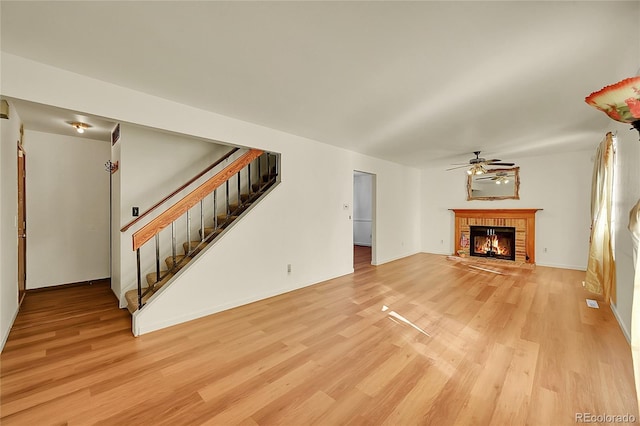 unfurnished living room with ceiling fan, a brick fireplace, and light wood-type flooring