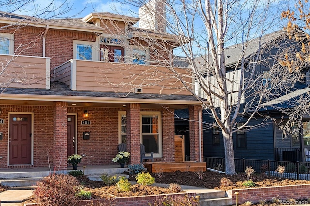 view of property featuring covered porch, brick siding, fence, and a chimney