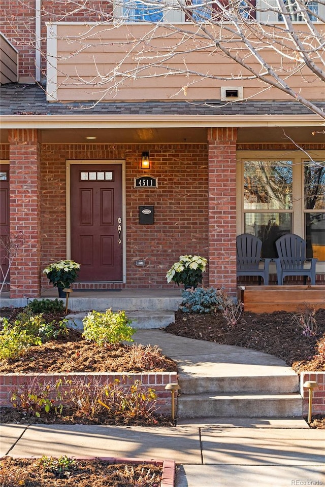 property entrance with covered porch, brick siding, and roof with shingles