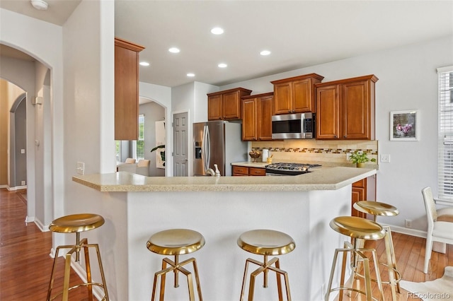 2605 Gray Wolf Loop, Broomfield, CO 80023 - kitchen with appliances with stainless steel finishes, arched walkways, a breakfast bar area, light countertops, and wood finished floors