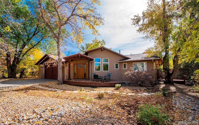 ranch-style home with a deck, driveway, an attached garage, and stucco siding