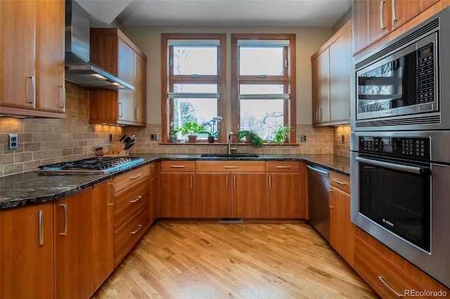 kitchen with stainless steel appliances, wall chimney exhaust hood, light wood-type flooring, and a sink