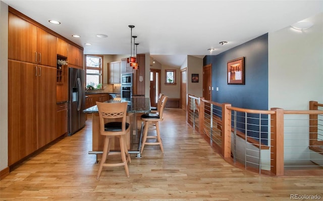 kitchen with brown cabinets, stainless steel microwave, light wood-style floors, a kitchen bar, and black fridge