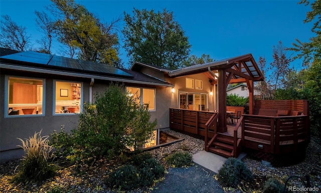 exterior space with roof mounted solar panels, a deck, and stucco siding