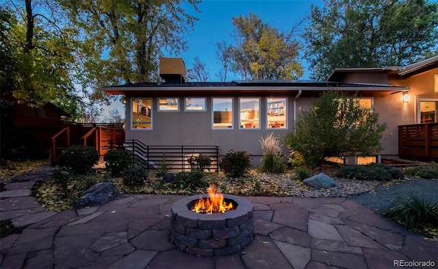 rear view of property featuring a patio, a fire pit, and stucco siding