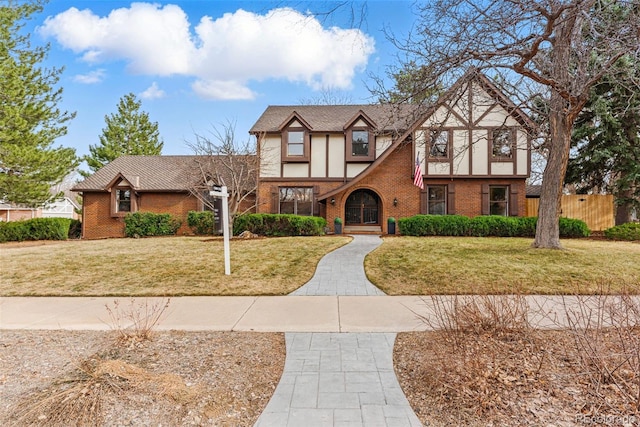 english style home featuring stucco siding, brick siding, a front lawn, and fence