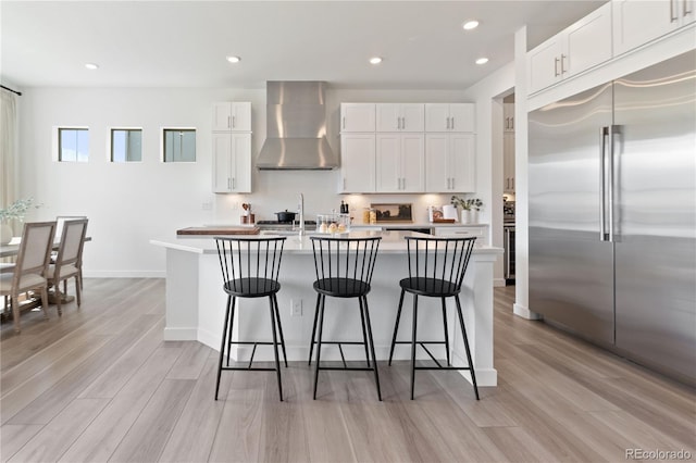 3147 S Quaker St, Morrison, CO 80465 - kitchen featuring wall chimney range hood, stainless steel built in refrigerator, light wood-style floors, an island with sink, and a breakfast bar