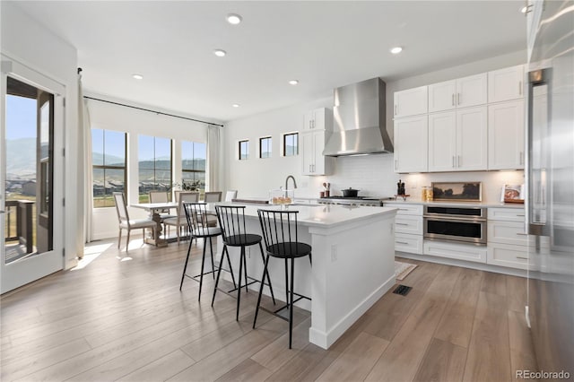 3147 S Quaker St, Morrison, CO 80465 - kitchen featuring wall chimney exhaust hood, oven, a kitchen island with sink, light countertops, and white cabinets