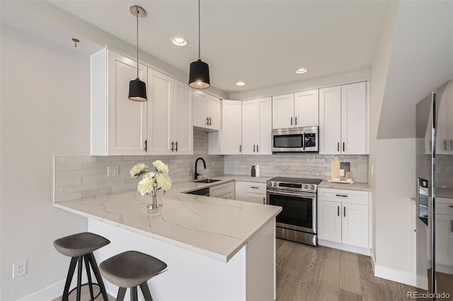 kitchen with a kitchen bar, light stone counters, appliances with stainless steel finishes, a peninsula, and a sink