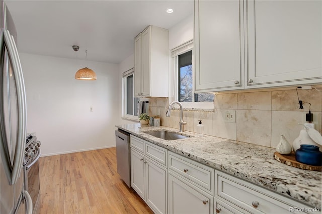 kitchen featuring sink, light stone counters, pendant lighting, appliances with stainless steel finishes, and light wood-type flooring