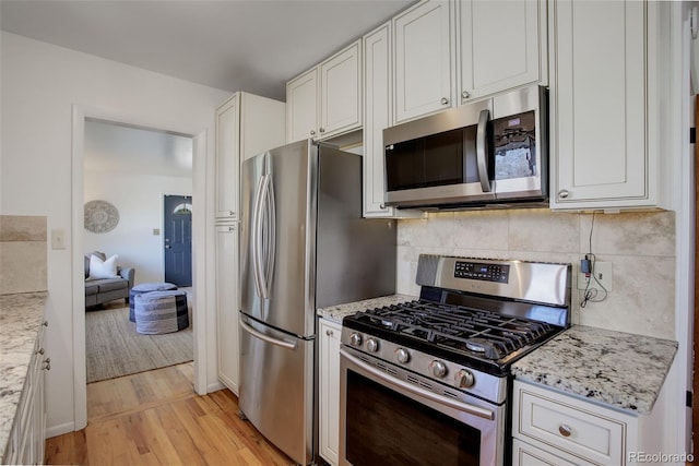 kitchen with white cabinets, light stone countertops, light wood-type flooring, and stainless steel appliances