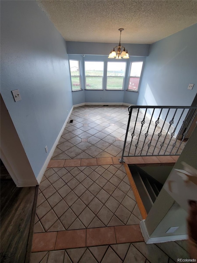 staircase featuring tile patterned flooring, healthy amount of natural light, a chandelier, and a textured ceiling