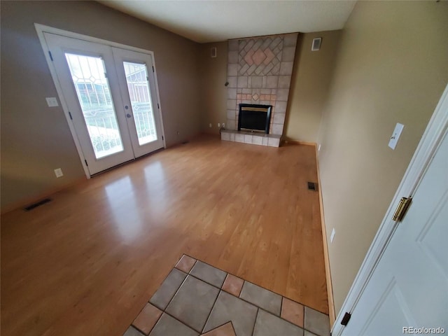 unfurnished living room featuring light wood-style floors, french doors, and a tile fireplace