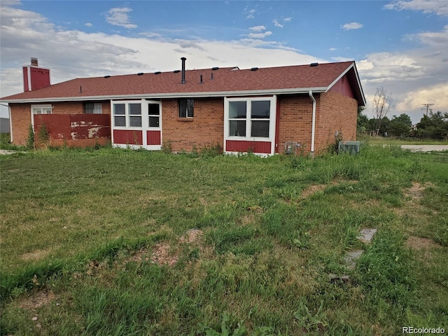 back of house with brick siding, a chimney, and a lawn