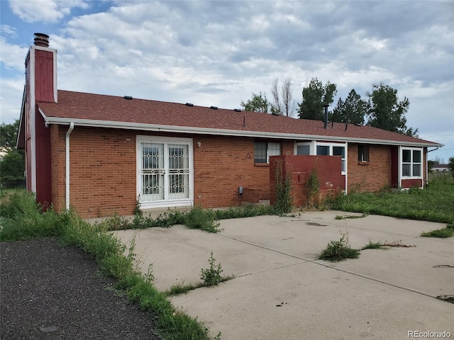 back of house featuring a chimney, brick siding, a patio, and roof with shingles