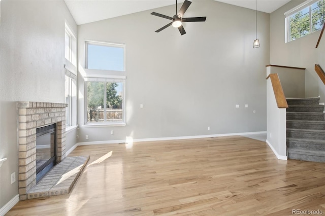 unfurnished living room featuring stairway, light wood-type flooring, a brick fireplace, high vaulted ceiling, and ceiling fan