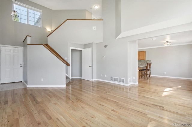 unfurnished living room featuring stairs, a towering ceiling, visible vents, and light wood-style flooring